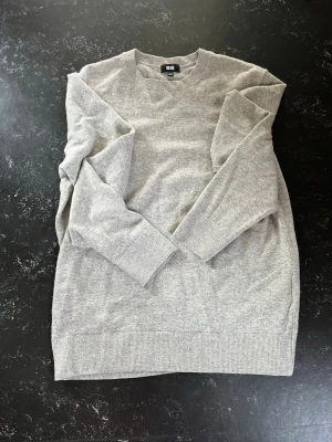 Ljusgrå kashmir tröja från Uniqlo - En stilren ljusgrå stickad tröja från Uniqlo med rund halsringning och långa ärmar. Tröjan har ribbade muddar vid ärmslut och nederkant. Perfekt basplagg i mjukt material som passar till det mesta.