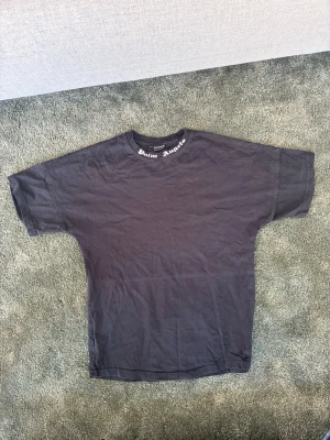 Svart oversized Palm Angels t-shirt - Svart oversized t-shirt från Palm Angels med logga i vit text på ryggen och mindre text runt halsringningen. Klassisk rund hals och korta ärmar. Tillverkad i mjuk bomull för en skön och avslappnad look.