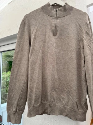 Beige halvzip tröja i viskosmix - Snygg beige tröja med halv dragkedja och hög krage. Tillverkad i mjuk viskosmix (65% viskos, 35% polyamid). Långärmad modell med ribbade muddar och avslut. Perfekt för en clean och avslappnad stil.