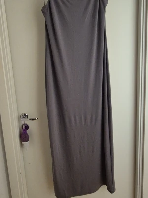Lång grå ärmlös klänning - En stilren långklänning i grått med enkel och rak passform. Klänningen är ärmlös och har en mjuk, slät yta som ger ett minimalistiskt intryck. Perfekt för dig som gillar en clean och tidlös look. Aldrig använd prislapp sitter kvar