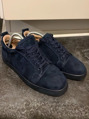 Mörkblå sneakers med röd sula - Snygga mörkblå sneakers i mocka med matchande blå skosnören och svart yttersula. Insidan är beige och sulan har en unik röd färg med mönster. Klassisk låg modell som passar till många olika stilar.