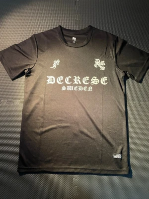 Svart decrese tröja LIMITED - Tröjan är limited eftersom decrese inte länge är uppe och har stängt ner butiken och online Snygg svart t-shirt från Decrese Sweden med vit tryckt text och logga framtill. Klassisk rund hals och korta ärmar. Tillverkad i ett mjukt och lätt material som känns skönt mot huden. Perfekt för dig som gillar streetwear och enkel stil.