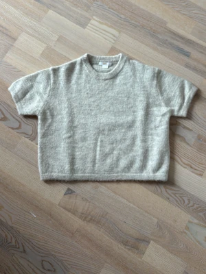 Beige stickad tröja Gina Tricot - Mysig beige stickad tröja från Gina Tricot med korta ärmar och rund halsringning. Tröjan har en enkel och avslappnad passform, perfekt för lager på lager och en chill look. Materialet är mjukt och fluffigt för extra komfort.