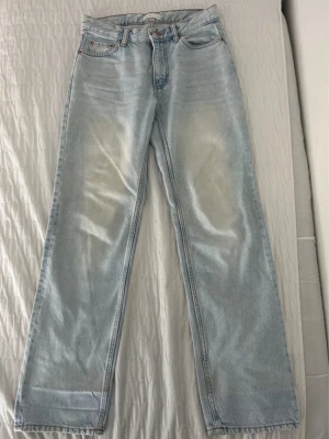 Ljusblå raka jeans, storlek 34 - Säljer ett par ljusblå jeans med rak passform och klassisk femficksdesign. Jeansen har en snygg tvättad look och är tillverkade i denim med kontrastsömmar. Perfekta för en avslappnad och trendig stil.