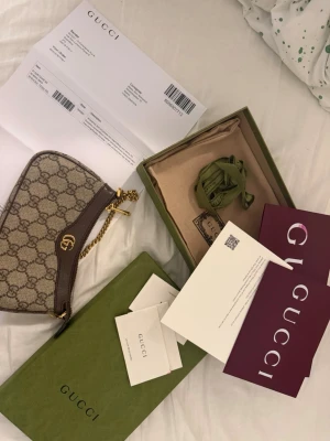 Gucci beige GG canvas handväska - Säljer en snygg beige handväska från Gucci i klassiskt GG canvasmönster med bruna läderdetaljer och guldfärgad kedja. Väskan har en elegant form och logga framtill. Kommer med originalkartong, dustbag och äkthetskort.