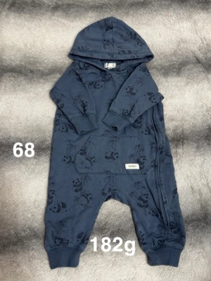 Mörkblå pandaoverall med huva - Mysig mörkblå overall med huva och tryckta pandamotiv. Overallen har långa ärmar, mudd vid ärmslut och benslut samt en stor magficka framtill. Dragkedja längs sidan för enkel påklädning. Perfekt för chill dagar hemma.🌸 Fint använt skick. Storlek 68 