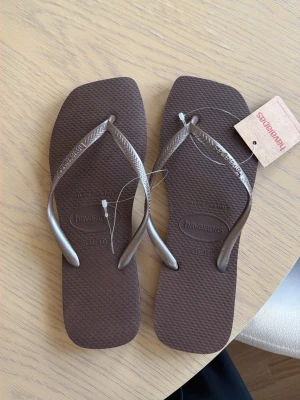 Bruna Havaianas sandaler - Snygga bruna sandaler från Havaianas med klassisk flip-flop design. Tillverkade i mjukt och flexibelt gummi med mönstrad sula och smala remmar i metallicbrunt. Perfekta för sommaren och stranden. Aldrig använt! Beställde fel storlek och åkte utomlands så hann inte skicka tillbaka! 