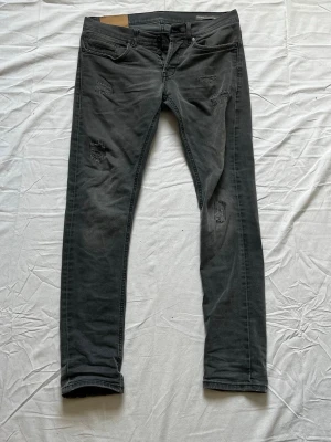 Grå Dondup jeans  - Säljer ett par grå skinny jeans med slitningar på låren och knäna. Jeansen har fem fickor, knappgylf och en tvättad look som ger en avslappnad vibe. Perfekta för dig som gillar en trendig och lite tuffare stil.