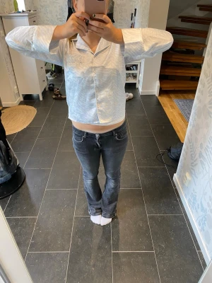 Ljusblå satinpyjamas med krage - Säljer en ljusblå pyjamaströja i satin med klassisk krage och knappar framtill. Tröjan har långa ärmar och en avslappnad passform, perfekt för mysiga kvällar hemma. Materialet är glansigt och mjukt mot huden.