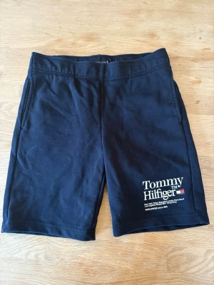 Svarta shorts från Tommy Hilfiger - Snygga svarta shorts från Tommy Hilfiger med tryckt logga på vänster ben och fickor både fram och bak. Tillverkade i mjuk bomull, perfekta för en avslappnad stil. Klassisk passform och elastisk midja för extra komfort.