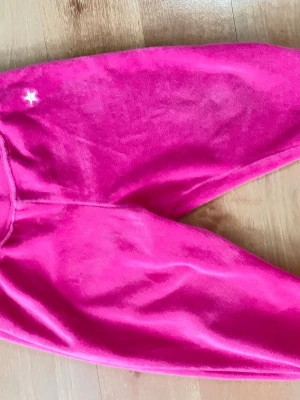 Rosa mjukisbyxor, Lindex, 92 - Ett par byxor i en stark rosa färg. Byxorna har resår i midjan och muddar vid bensluten. På ena benet finns en liten vit stjärna broderad.