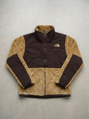 Brun teddyjacka från The North Face - Säljer en snygg teddyjacka från The North Face i brunt och beige. Jackan har hög krage, dragkedja framtill och två fickor med dragkedja. Materialet är mjukt teddytyg med förstärkta partier på bröst och ärmar. Perfekt för kalla dagar.