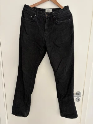 Svarta raka jeans från Skagen  - Säljer ett par svarta jeans från Skagen med rak passform och klassisk femficksdesign. Jeansen har hög midja och är gjorda i kraftigt denimtyg. Perfekta för en clean och stilren look. Saknar knappen i fram men bra skick i övrigt! Passar dig som är runt 180cm.
