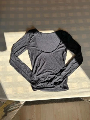 Topp med öppen rygg - En enkel och stilren mörkblå långärmad topp med rund, djup ringning bak. Tunn och mjuk i materialet, perfekt att styla lager på lager eller bära som den är. Passformen är ganska tight.