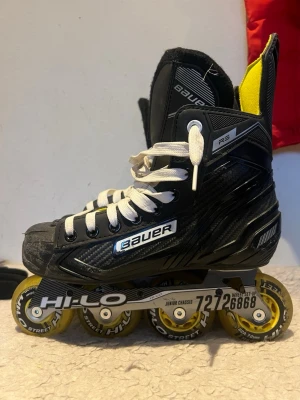 Bauer R5 inlines med gula hjul - Säljer ett par svarta Bauer R5 inlines med vita snören och gula hjul. Skorna har en sportig design med detaljer i silver och gult foder på insidan. Hjuluppsättningen är Hi-Lo och passar perfekt för street och hockeyträning.