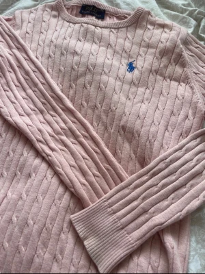 Ljusrosa kabelstickad tröja Polo Ralph Lauren - Helt ny, fraktar inom 8 h, öppen för prisförslag Ljusrosa kabelstickad tröja från Polo Ralph Lauren med rund halsringning och blå broderad logga på bröstet. Tröjan har långa ärmar och ribbade muddar vid ärmslut och nederkant. Klassisk och tidlös design i mjukt material.