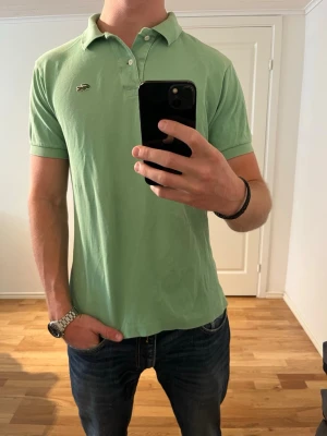 Ljusgrön Lacoste piké  - Säljer denna sjukt snygga pikén från Lacoste⭐️ Färgen är ljusgrön och storleken är M✅ Den har inga defekter och skicket är utomordentligt🙌🤝 Sjukt najs passform och passar perfekt till hösten☀️🙌 Tveka inte på att höra av er dig vid minsta fråga eller fundering😊