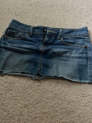 Blå jeanskjol Espirit  - Kort jeanskjol i blå denim med rå kant och slitningar. Kjolen har fem fickor och snygga broderade detaljer på bakfickorna. Perfekt för dig som gillar en avslappnad och trendig stil.