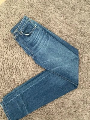 Blå jeans från Djerf Avenue - Säljer ett par jeans från Djerf Avenue. Lösare/rak passform, midwaisted med fin brodering bak på fickan. Något slitna längst ner på byxbenet, annars utan defekter. Storlek 26 tall, nypris 1500 kr. 