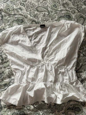Vit peplumtop från Gina Tricot💓 - Snygg vit peplumtop från Gina Tricot med v-ringning och korta ärmar. (Bara andvänt den nån enstaka gång, materialet är väldigt plastigt vilket gör att den bli skrynklig lätt)