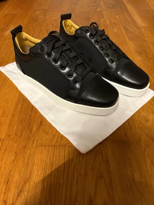 Louboutin sneakers utan spikar HELT NYA - Stilrena svarta sneakers med vit mellansula och en cool röd undersida. Skorna har svarta skosnören, diskret design och insida i beige. Och dessa är helt nya utan spikar