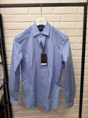 Ljusblå slim fit skjorta från MNG - Snygg ljusblå skjorta från MNG i slim fit-modell. Skjortan har klassisk krage, långa ärmar och knappar framtill. Perfekt för dig som gillar en stilren och enkel look. Tillverkad i ett lätt och bekvämt material.