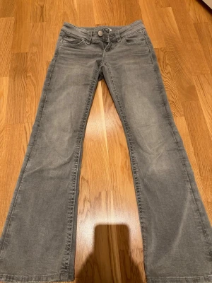 Grå bootcut jeans med fickdetaljer - Säljer ett par gråa bootcut jeans med snygga fickdetaljer bak. Jeansen har låg midja. Perfekta till en trendig vardagslook och passar till det mesta. Materialet är mjukt och stretchigt för extra komfort.