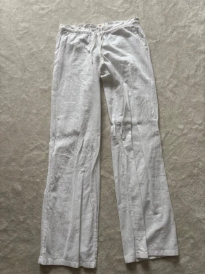 Vita vida linnebyxor med resårmidja - Säljer ett par klassiska vita linnebyxor med avslappnad passform och resår i midjan. Byxorna har raka, vida ben och sidfickor. Perfekta för en chill och stilren look under varma dagar.