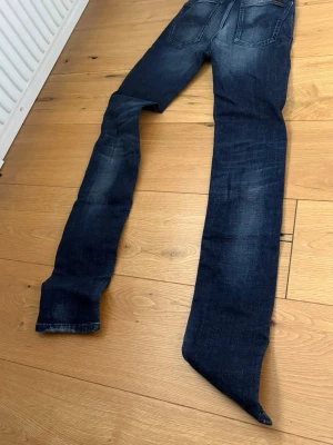 Mörkblå skinny jeans med slitningar - Säljer ett par mörkblå skinny jeans med snygga slitningar och tvättade detaljer på benen. Jeansen har klassisk femficksmodell och smal passform hela vägen ner. Perfekta för dig som gillar en tajt look och vill ha ett par jeans som känns trendiga.