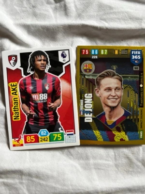 Fotbollssamlarbilder FIFA 365 - Två fotbollssamlarbilder med spelarna Nathan Aké och Frenkie de Jong. Korten har färgstarka designer med klubbmärken, spelarstatistik och namn. Perfekta för dig som gillar att samla på fotbollskort och vill ha något unikt till din samling.