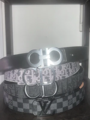 Valfritt bälte  - Fyra snygga bälten i svart och grått med olika mönster och coola metallspännen. Ett bälte är helsvart, två har monogrammönster och ett har rutigt mönster. Perfekta accessoarer för att lyfta din outfit.