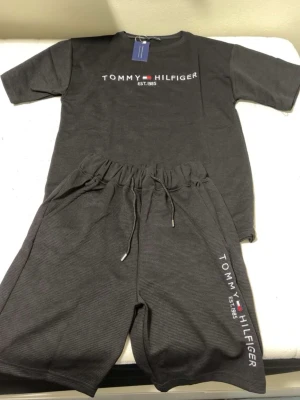 Svart set från Tommy Hilfiger - Snyggt svart set från Tommy Hilfiger med t-shirt och shorts. Båda delarna har logga och texten 'EST. 1985' framtill. Materialet är mjukt och har en diskret struktur. Shortsen har resår och dragsko i midjan för skön passform.