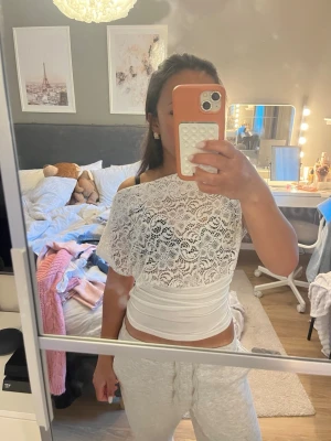 Vit spetsblus med omlott och offshoulder - Säljer en vit blus med spets upptill och omlott-detalj i midjan. Toppen har offshoulder-design och är ärmlös, vilket ger en fräsch och trendig look. Perfekt för dig som vill ha något extra till outfiten!