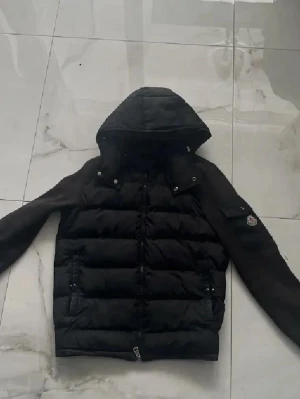 Svart dunjacka med huva - Snygg svart dunjacka från Moncler med quiltad kropp, släta ärmar och avtagbar huva. Jackan har dragkedja framtill, två sidofickor med dragkedja och Moncler-logga på ena ärmen. Perfekt för kalla vinterdagar. Du kan också ta av luvan 