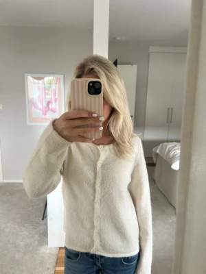 Vit fluffig kofta med knappar - Mysig vit kofta med fluffig känsla och rund halsringning. Koftan har långa ärmar och stängs med små vita knappar framtill. Passar perfekt till jeans eller över ett linne för en enkel och stilren look.