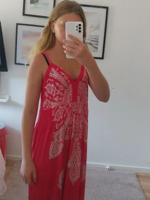 Rosa sommarklänning med mönster från Thailand  - Säljer en risa klänning med vita detaljer och tunna axelband. Klänningen har ett snyggt bohemiskt mönster och v-ringad hals. Perfekt för varma dagar och har en avslappnad passform som ger en skön känsla. Den är i  från Thailand 