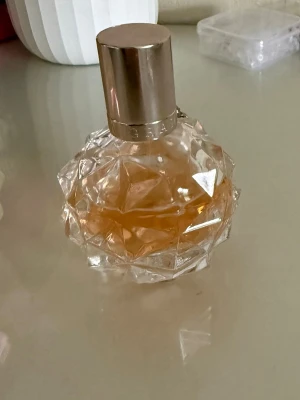 Ariana grande parfym  - Säljer en parfym i en unik, kristalliknande glasflaska med geometriskt mönster. Flaskan har en guldig metallkork och innehållet är bärnstensfärgat. Perfekt för dig som gillar snygg design på parfymflaskor.