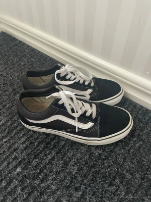 Svarta Vans sneakers - Klassiska Vans Old Skool sneakers i svart med vit sula och vit sidostripes. Skorna har vita skosnören och kontrastsömmar. Ovandelen är i mocka och canvas vilket ger en snygg och tidlös look.