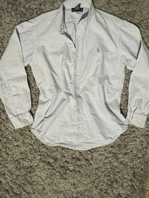 Randig skjorta från Polo Ralph Lauren - Ralph Lauren skjorta - Storlek 12  Säljer en stilren Ralph Lauren-skjorta i storlek 12. Använd endast 5-6 gånger, så den är i mycket fint skick och känns nästan som ny. Hör gärna av dig om du vill ha fler bilder eller har frågor.
