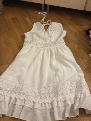 Vit spetsklänning från Boture XS - Söt vit kortklänning från Boture i storlek XS. Klänningen har v-ringning, spetsdetaljer, volangkant och knytband i nacken. Perfekt för sommarens alla tillfällen och har en romantisk look med broderade detaljer.