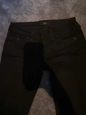 Svarta bootcut jeans  - Säljer ett par svarta bootcut jeans med klassisk femficksdesign och hällor för bälte. Jeansen har en tight passform och är tillverkade i ett stretchigt material som sitter snyggt. Perfekta till en avslappnad eller trendig look.