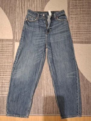 Blå raka jeans med hög midja - Säljer ett par klassiska blå jeans med rak passform och hög midja. Jeansen har fem fickor, gylf med dragkedja och knapp samt dubbla bakfickor. Materialet är kraftig denim i 100% bomull. Perfekta för en avslappnad och trendig look.
