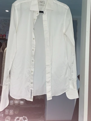 Vit klassisk skjorta med knappar - Säljer en stilren vit skjorta med lång ärm och klassisk krage. Skjortan har knäppning framtill och är tillverkad i ett mjukt bomullstyg. Perfekt för en clean och enkel look.