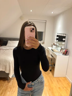 Svart långärmad topp - Säljer en enkel och stilren svart långärmad topp med rund hals. Toppen har en tight passform och är tillverkad i ett stretchigt material som sitter snyggt på kroppen. Perfekt att matcha med jeans eller kjol för en clean look.