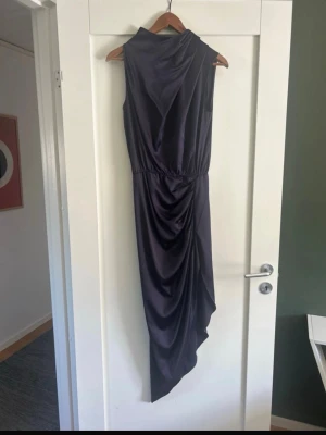 Mörklila långklänning i satin - Från Ahlvar Gallery. Använd en gång, i väldigt fint skick. True to size, så funkar om du är xs/s i vanliga fall.  Beskrivning av klänningen:   Tilda-klänningen är sydd i en blandning av acetat och stretchmaterial med en satinliknande yta. Den har asymmetriska veck som skapar ett vackert draperat fall vid halsringningen samt en dold dragkedja i nacken.  Den perfekta klänningen för festligheter.  Ordinarie pris 1995 kr.