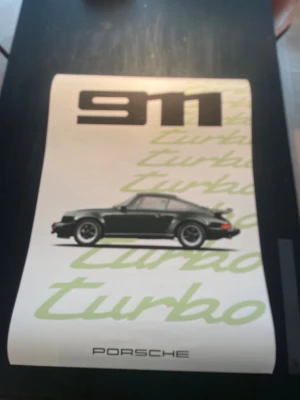 Porsche 911 affischer - Två snygga affischer med motiv av Porsche 911. Den ena har en klassisk svart Porsche 911 Turbo med gröna detaljer och text, den andra visar en modern silverfärgad Porsche 911 med röda fälgar och racingränder på vinröd bakgrund. Perfekt för bilälskare och väggdekoration.