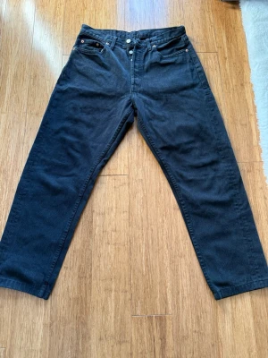 Levi’s - Säljer ett par svarta jeans med rak passform och hög midja. Klassisk femficksmodell med knappgylf och silverfärgade nitar. Jeansen har en enkel och tidlös look som passar till det mesta. Materialet är kraftig denim i bomull. Lite oversized look, W 33 L 32