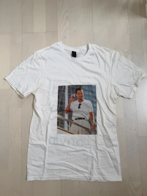 Vit t-shirt med tryck och text - Egen designad Vit t-shirt med tryck framtill av en man i vit outfit och svart text på ryggen: 'Need Money For Lanvin'. Kostade mig 700kr. Klassisk passform och rund halsringning. Perfekt för dig som gillar statement-plagg och streetstyle .