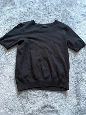 Svart kortärmad topp från H&M - En enkel och stilren svart topp från H&M med korta ärmar och rund halsringning. Tillverkad i mjuk bomull som känns skön mot huden. Perfekt att matcha med jeans eller kjol för en clean look.