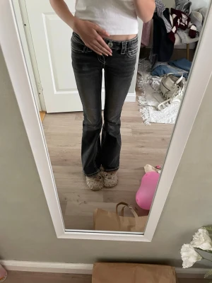 Svarta bootcut jeans med vita sömmar - Säljer ett par svarta bootcut jeans med tydliga vita kontrastsömmar och snygga detaljerade bakfickor. Jeansen har låg midja och klassisk femficksdesign. Perfekta för dig som gillar en retro vibe och vill sticka ut lite extra.